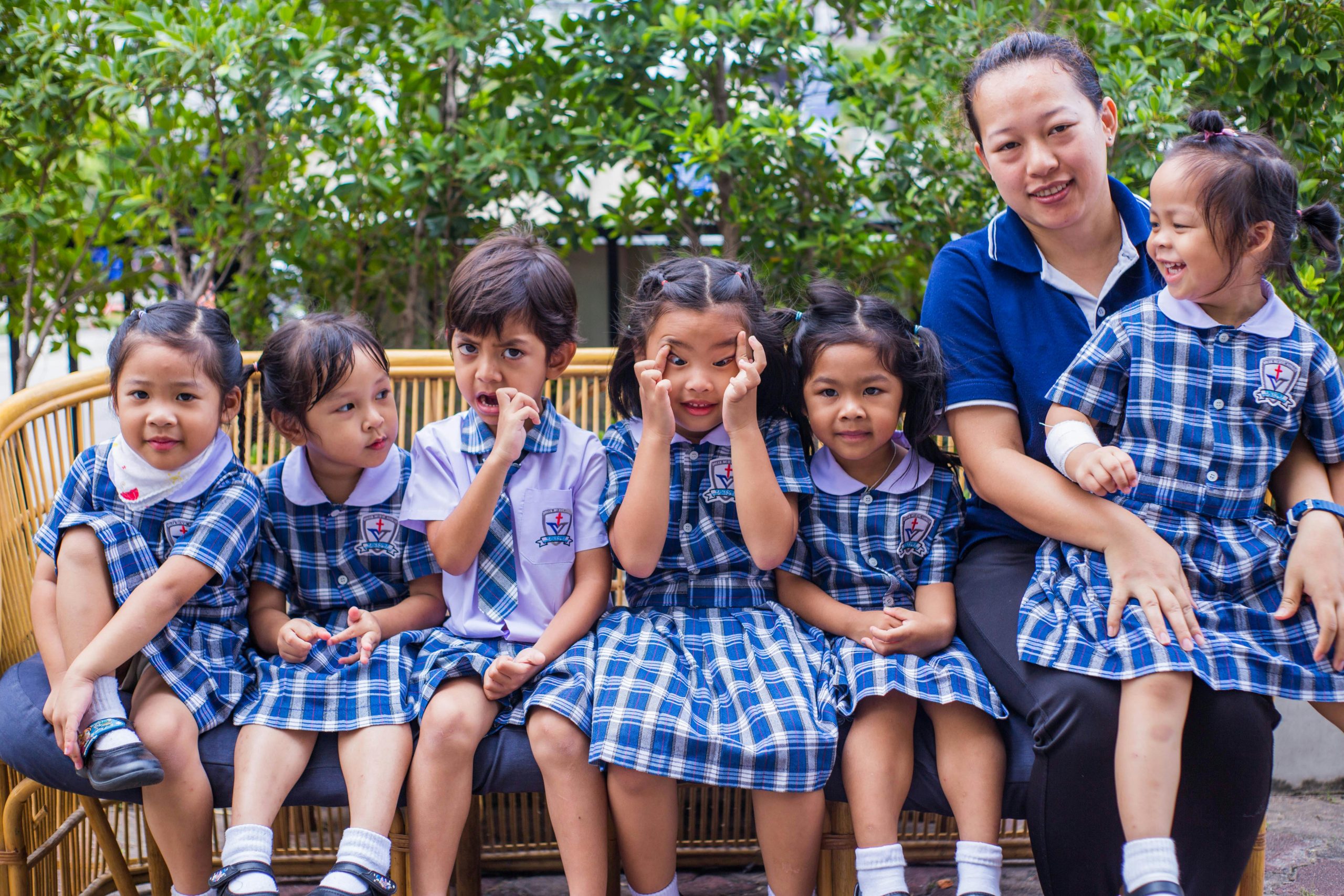 Happy children in school uniforms sitting together outdoors with a caregiver.